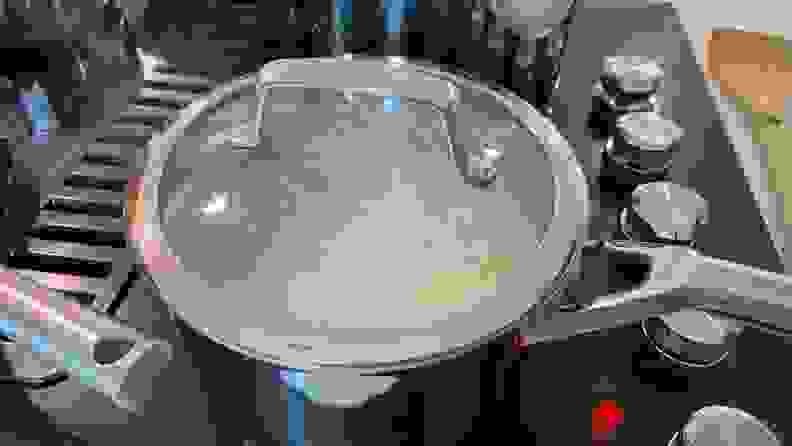 Rice being cooked inside a stainless steel pot, that's on top of a black stove top.